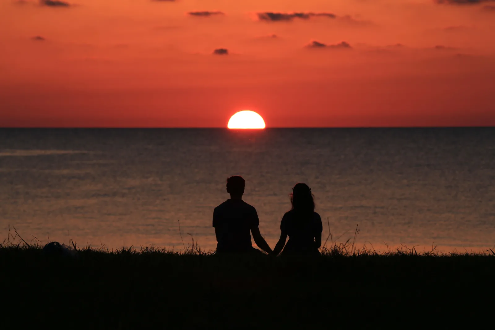 Casal em silhueta de mãos dadas observando o pôr do sol no horizonte