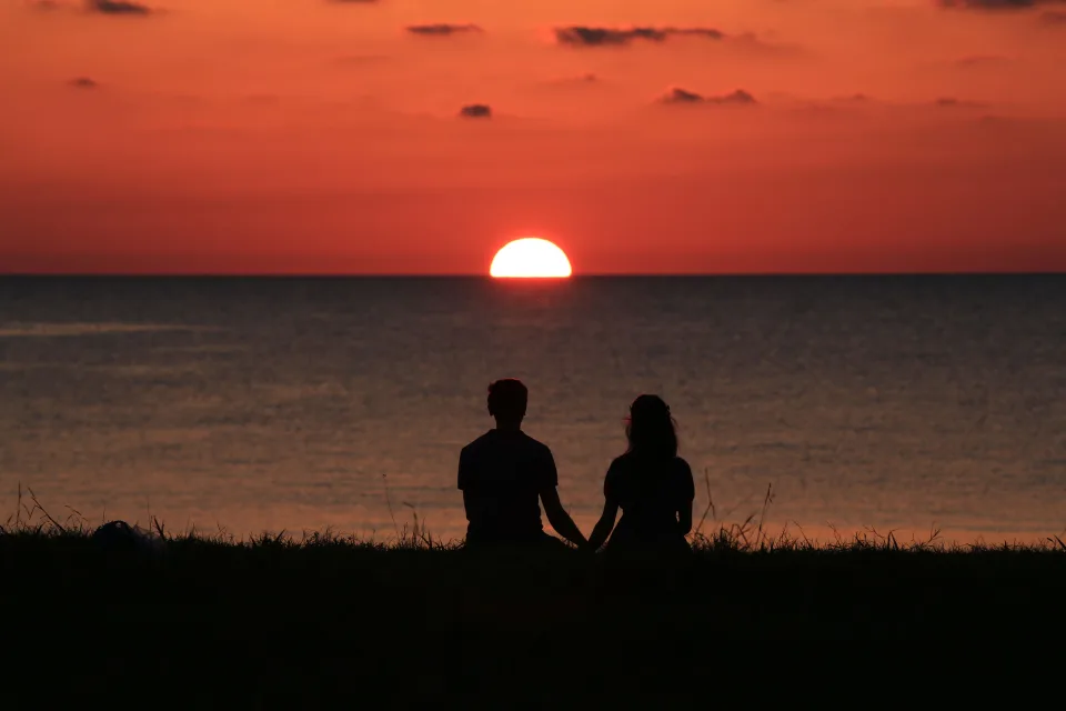 Casal em silhueta de mãos dadas observando o pôr do sol no horizonte
